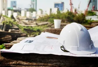 Casque de chantier blanc et plans de masse déposés sur un site de construction Nexa Energy Africa en préparation d'une installation énergétique.