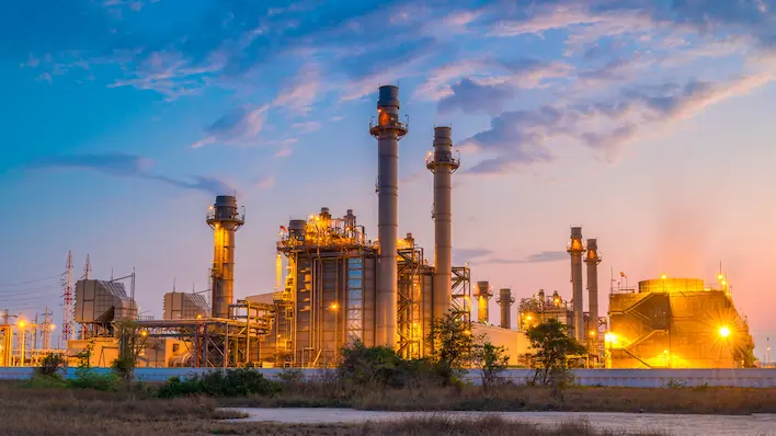 Centrale industrielle avec hautes cheminées et installations énergétiques éclairées au crépuscule.